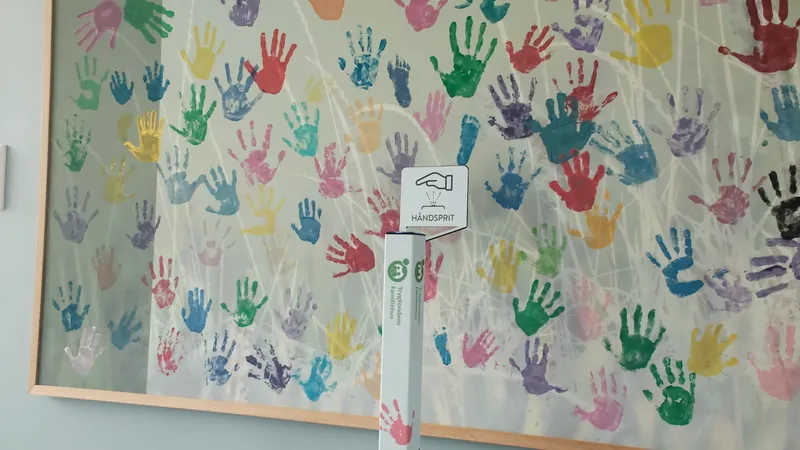 A Geysier dispenser in front of a wall of colourful children's handprints at Børnefonden